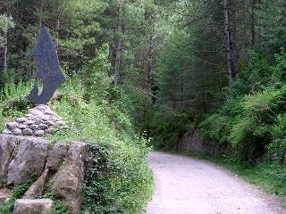 Vista de l'antiga explanació del tren, avui convertit en camí, amb l'escultura dedicada a la truita de riu